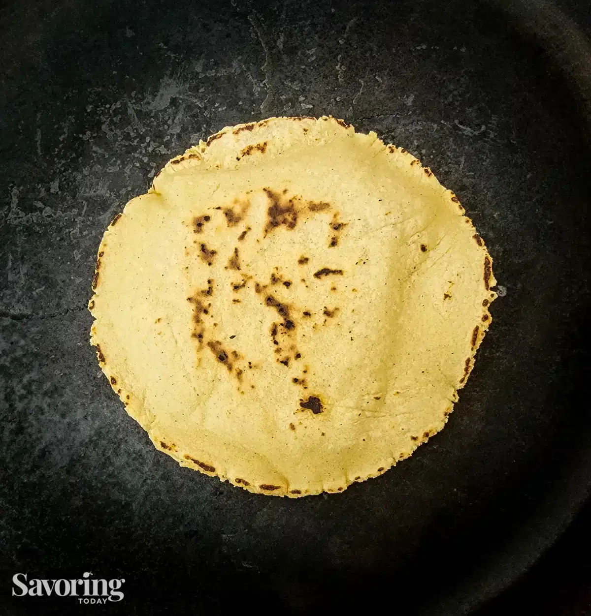 A cooked corn tortilla on a black cast iron skillet