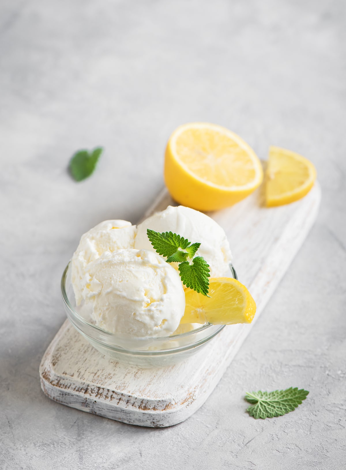 Lemon ice cream in a clear bowl on a white cutting board with lemon slices