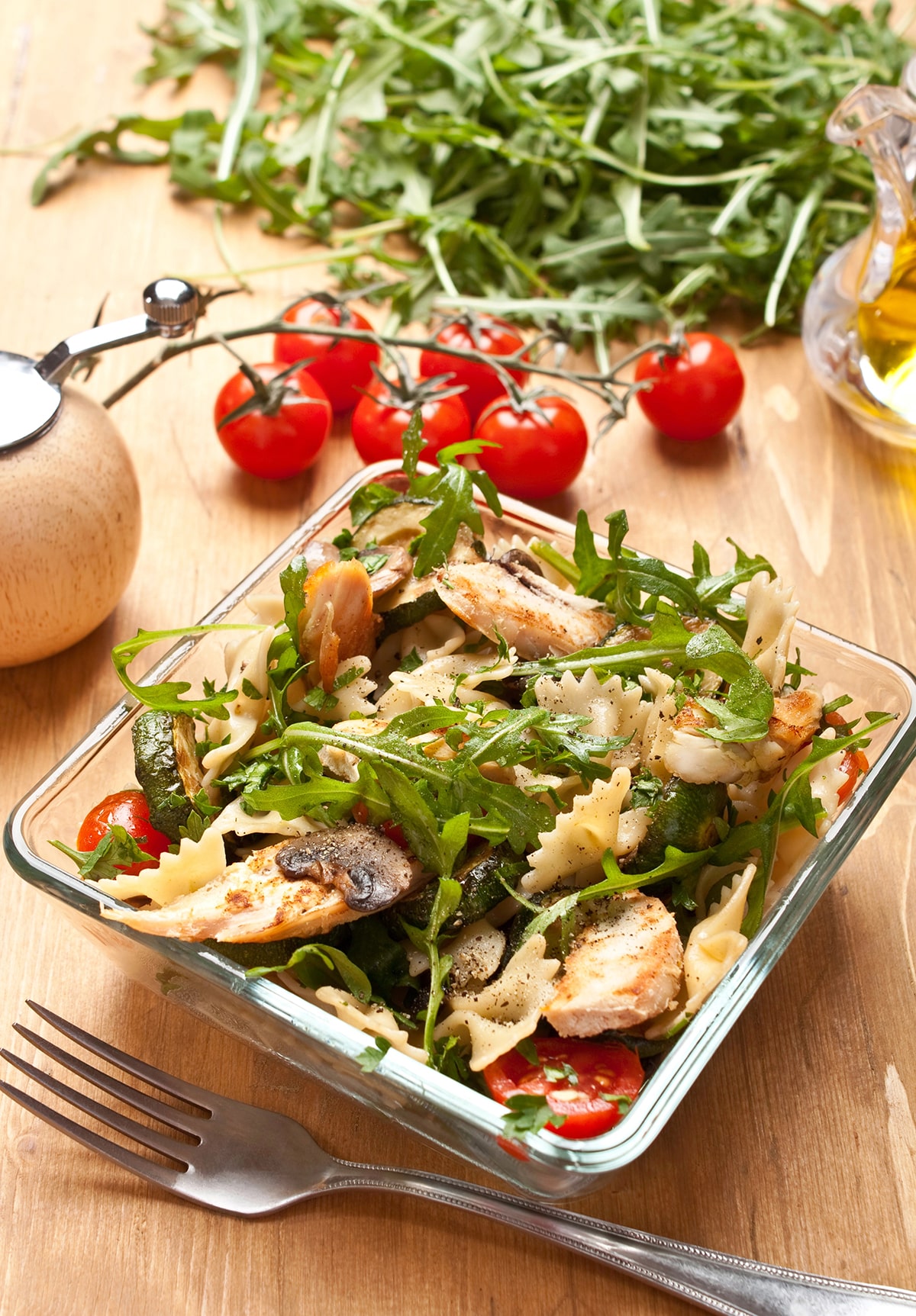 pasta salad in a clear square container with arugula and chicken