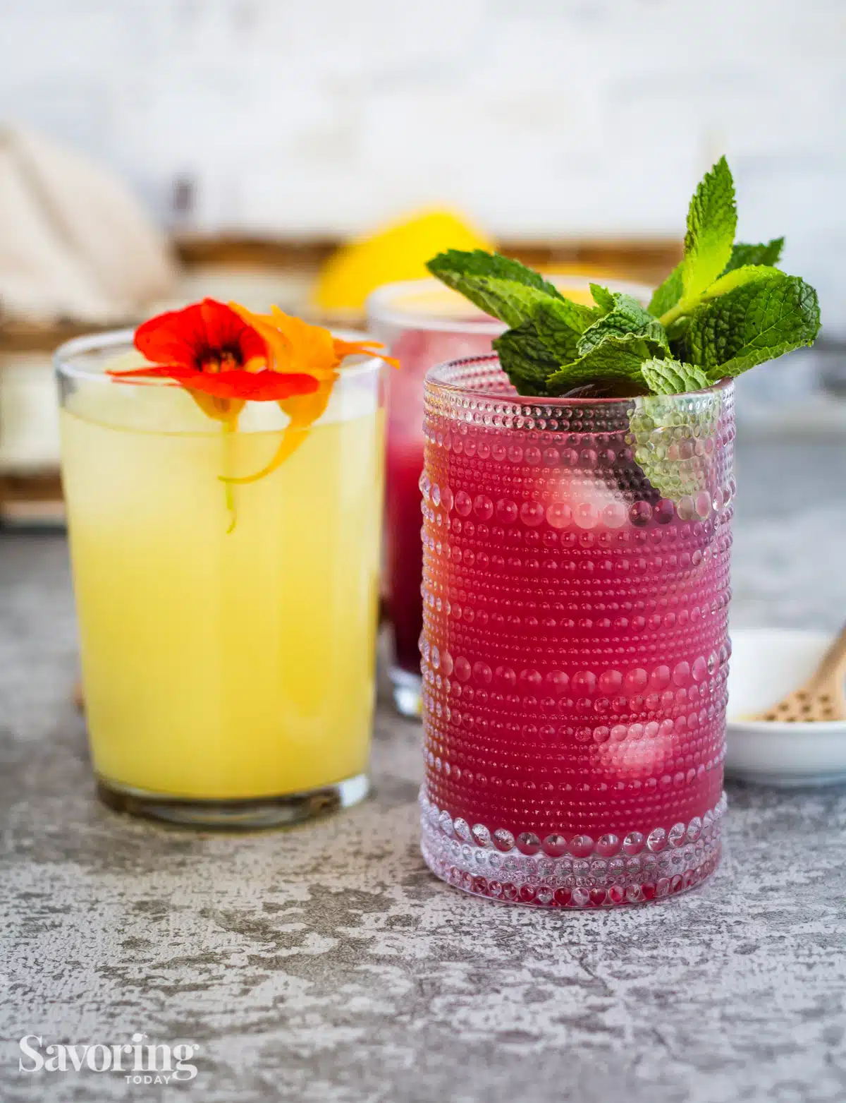 ginger lemon switchel garnished with flowers and mint on a grey counter