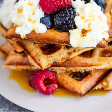 whole wheat waffles with whipped cream, berries, and syrup on a white plate