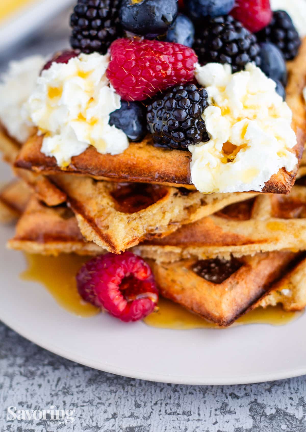 whole wheat waffles with whipped cream, berries, and syrup on a white plate