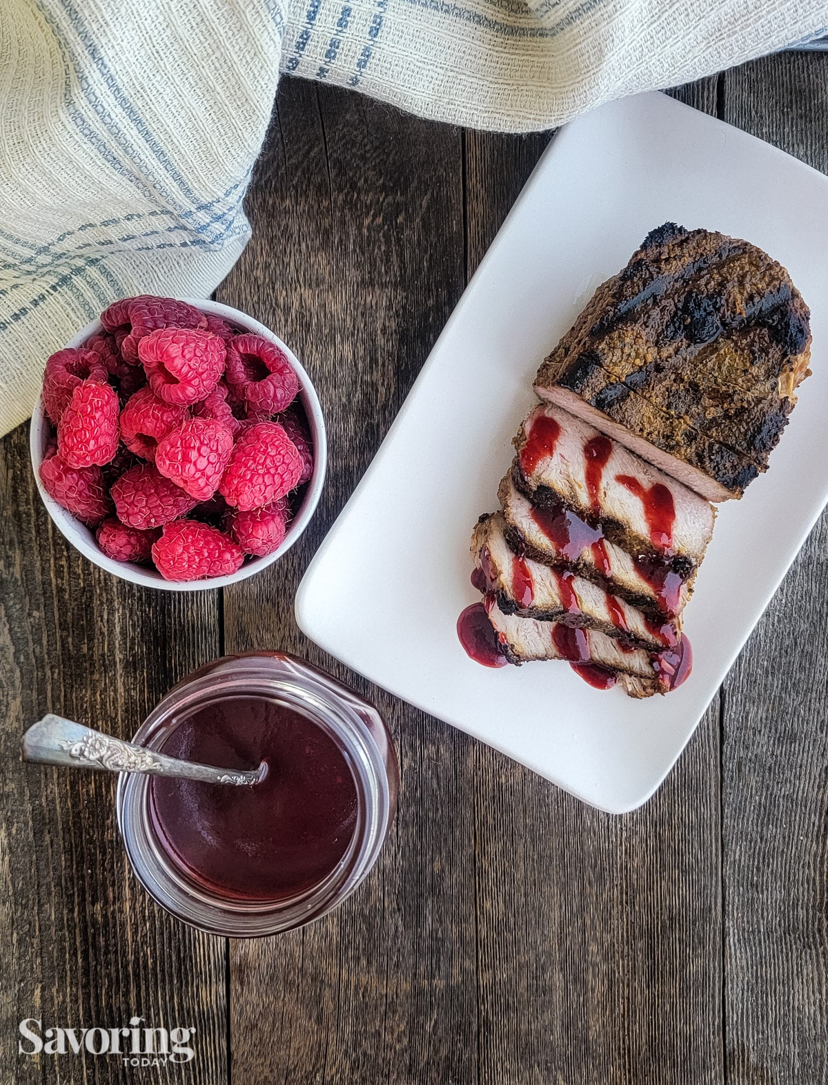 pork drizzled with raspberry sauce on a white plate beside fresh raspberries