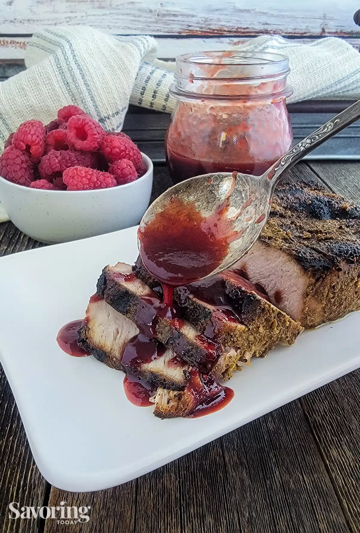 Sliced grilled pork chop on a white plate with raspberry chipotle sauce spooned over it.