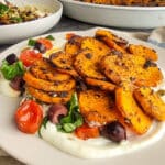 roasted sweet potates on whipped ricotta with tomatoes and olives on a tan plate beside casserole dishes