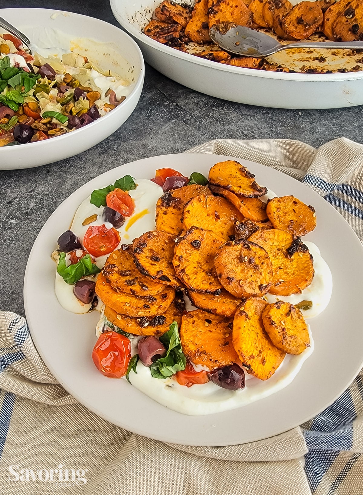 Roasted sweet potatoes served over whipped ricotta dip on a tan plate sitting on a tea towel