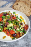 Savory ricotta feta dip with tomatoes, artichoke hearts, and olives in a white bowl