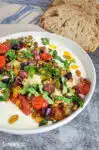 Savory ricotta feta dip with tomatoes, artichoke hearts, and olives in a white bowl
