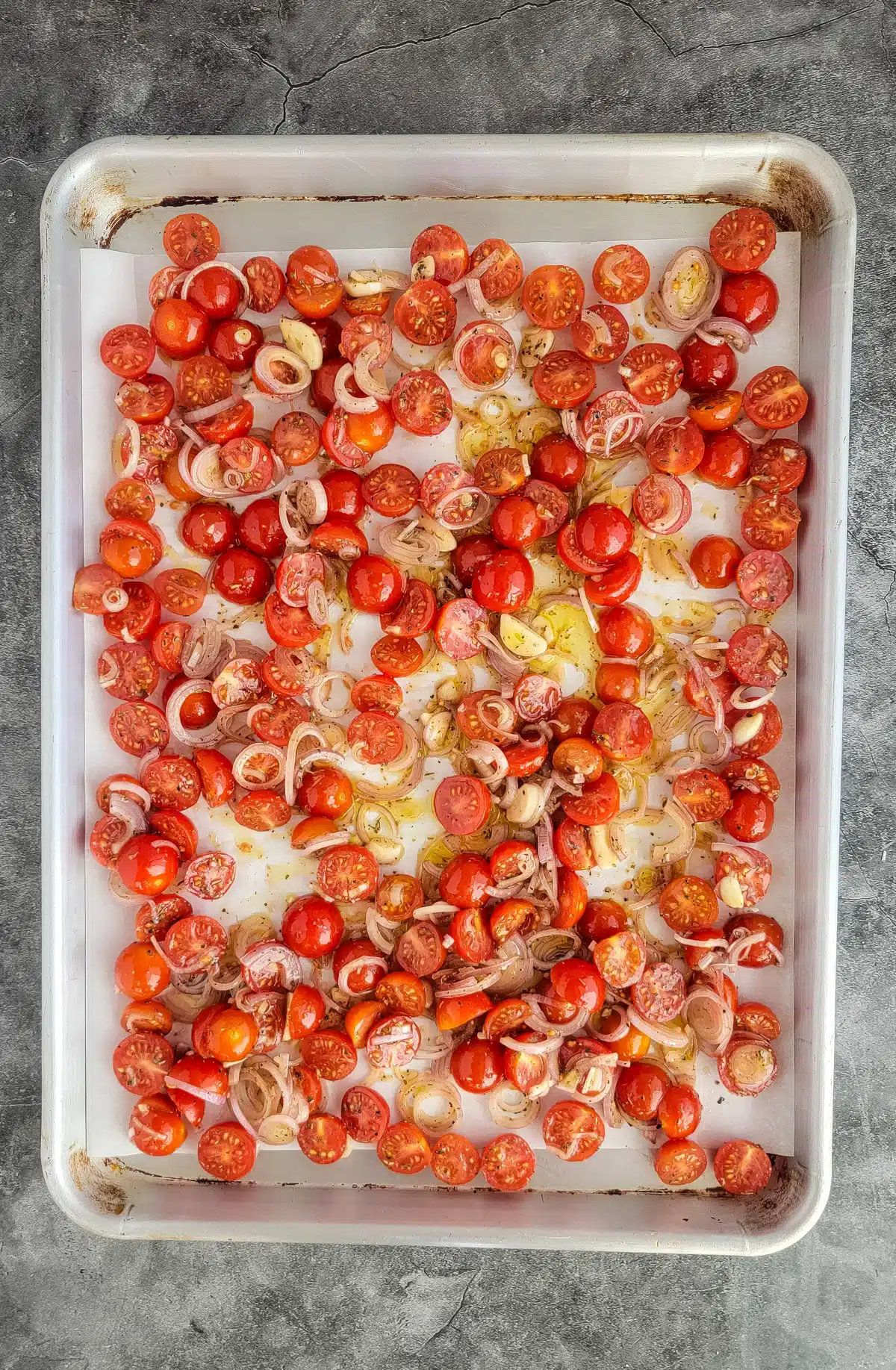Roasted tomatoes and shallots on a pan.