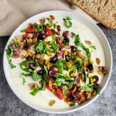 Savory ricotta feta dip in a white bowl with bread on a counter ready to serve