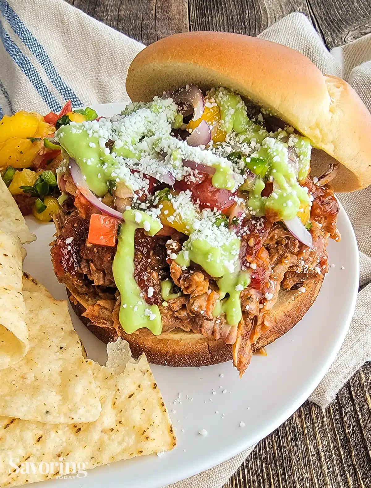 Al pastor pulled pork sandwich on a white plate with chips