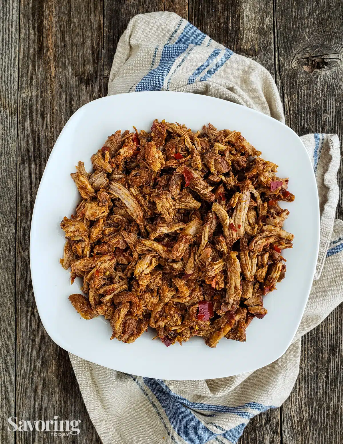 Pulled pork on a white plate set on a towel.