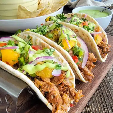 Pulled pork tacos lined up on a wood cutting board.