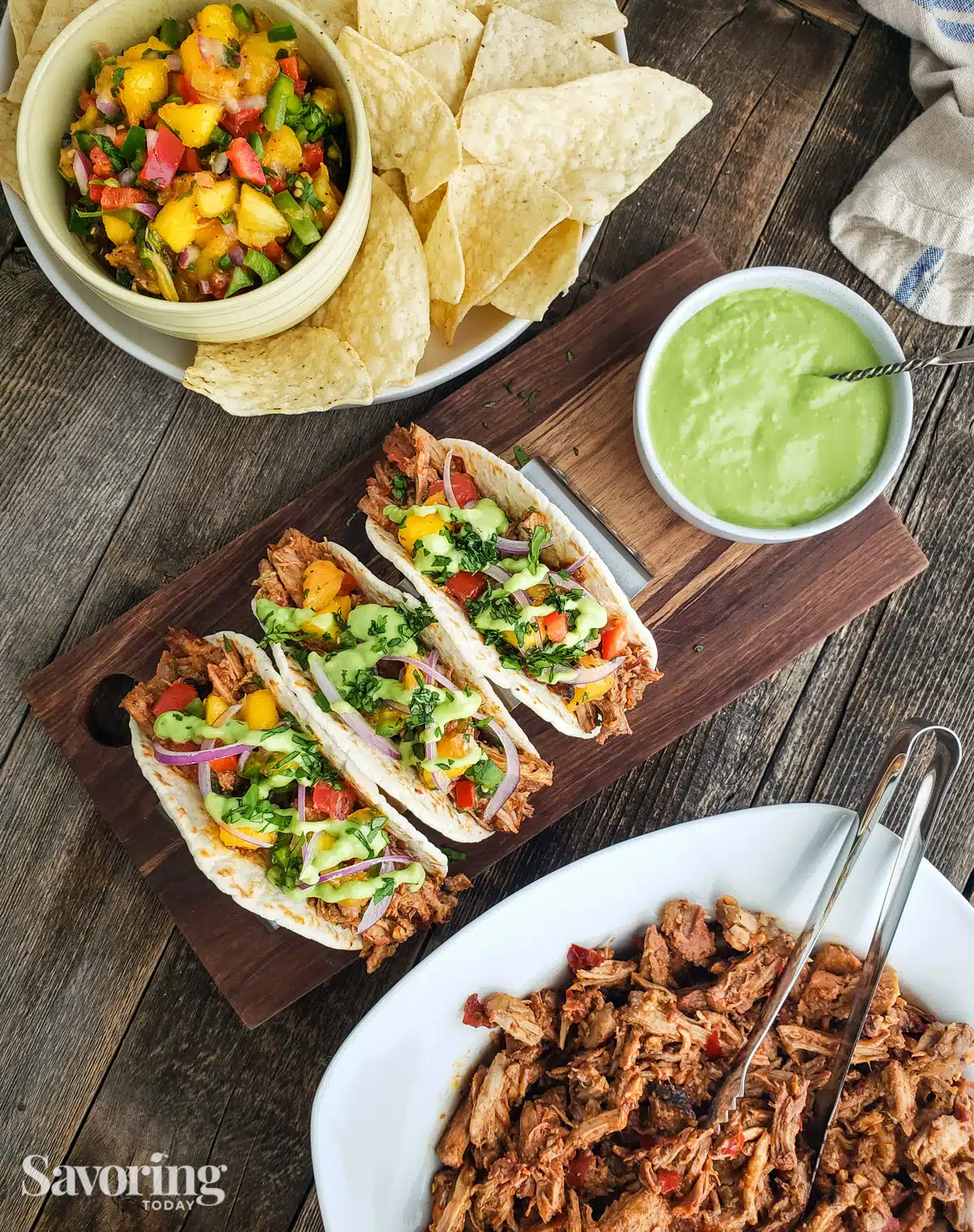 pork tacos on table with salsa, crema, and a bowl of pork
