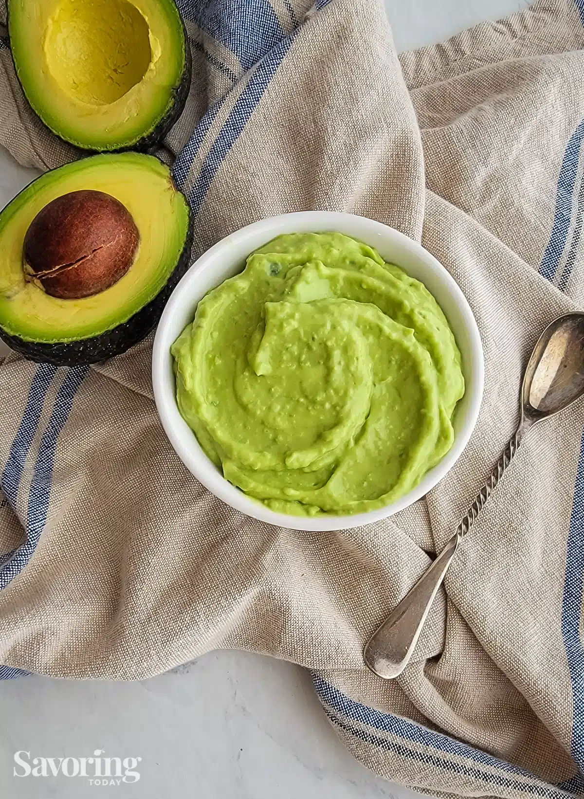 avocado crema in a light grey bowl with a spoon on a towel