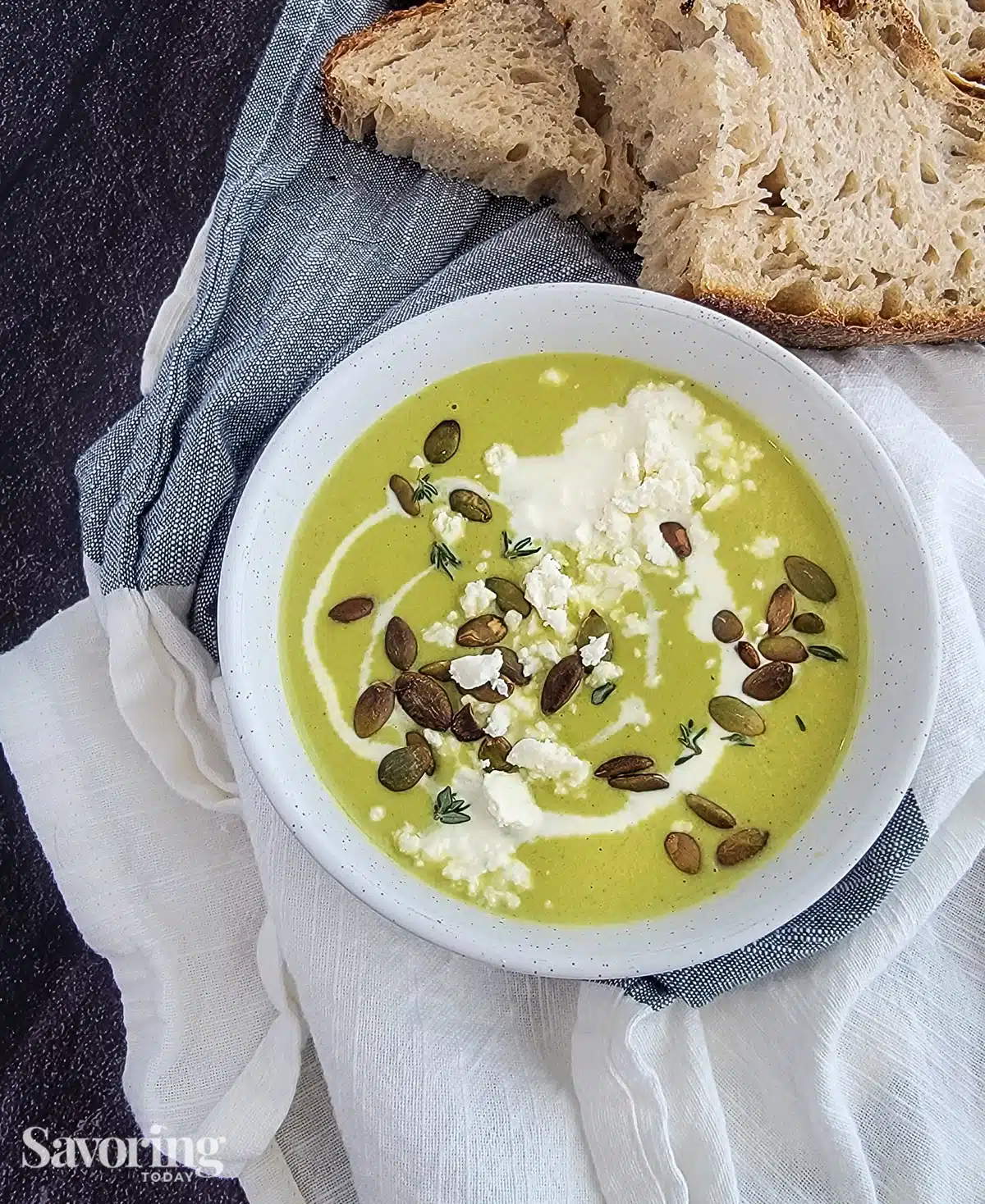Asparagus soup with pepitas and feta cheese in a white bowl with bread
