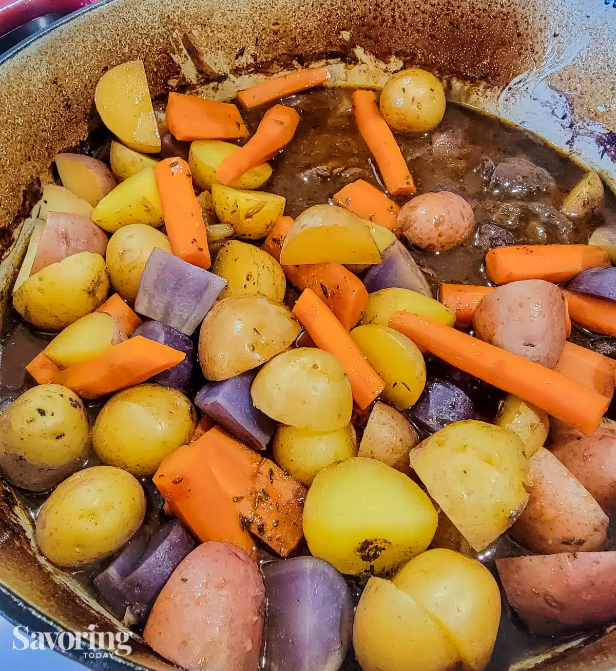 potatoes and carrots resting on top of pot roast in a Dutch oven