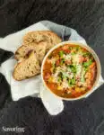 Italian sausage and split pea stew in a white bowl set on a towel with rustic bread