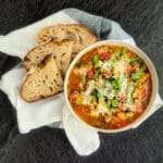 Italian sausage and split pea stew in a white bowl set on a towel with rustic bread