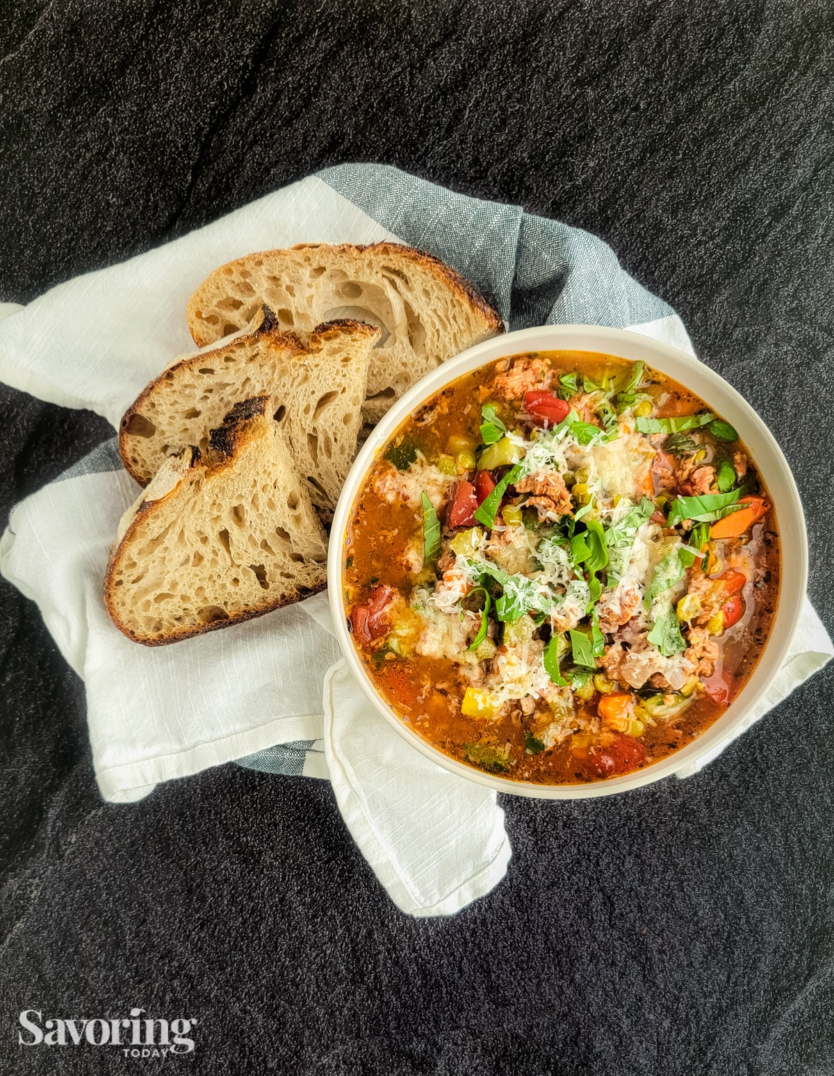 Italian sausage and split pea stew in a white bowl set on a towel with rustic bread