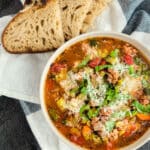 Italian sausage and split pea stew in a white bowl with bread on a towel