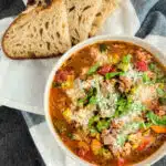 Italian sausage and split pea stew in a white bowl with bread on a towel
