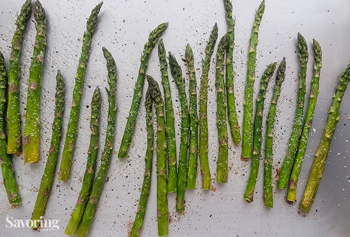 roasted asparagus seasoned with salt and pepper on a rimmed baking sheet