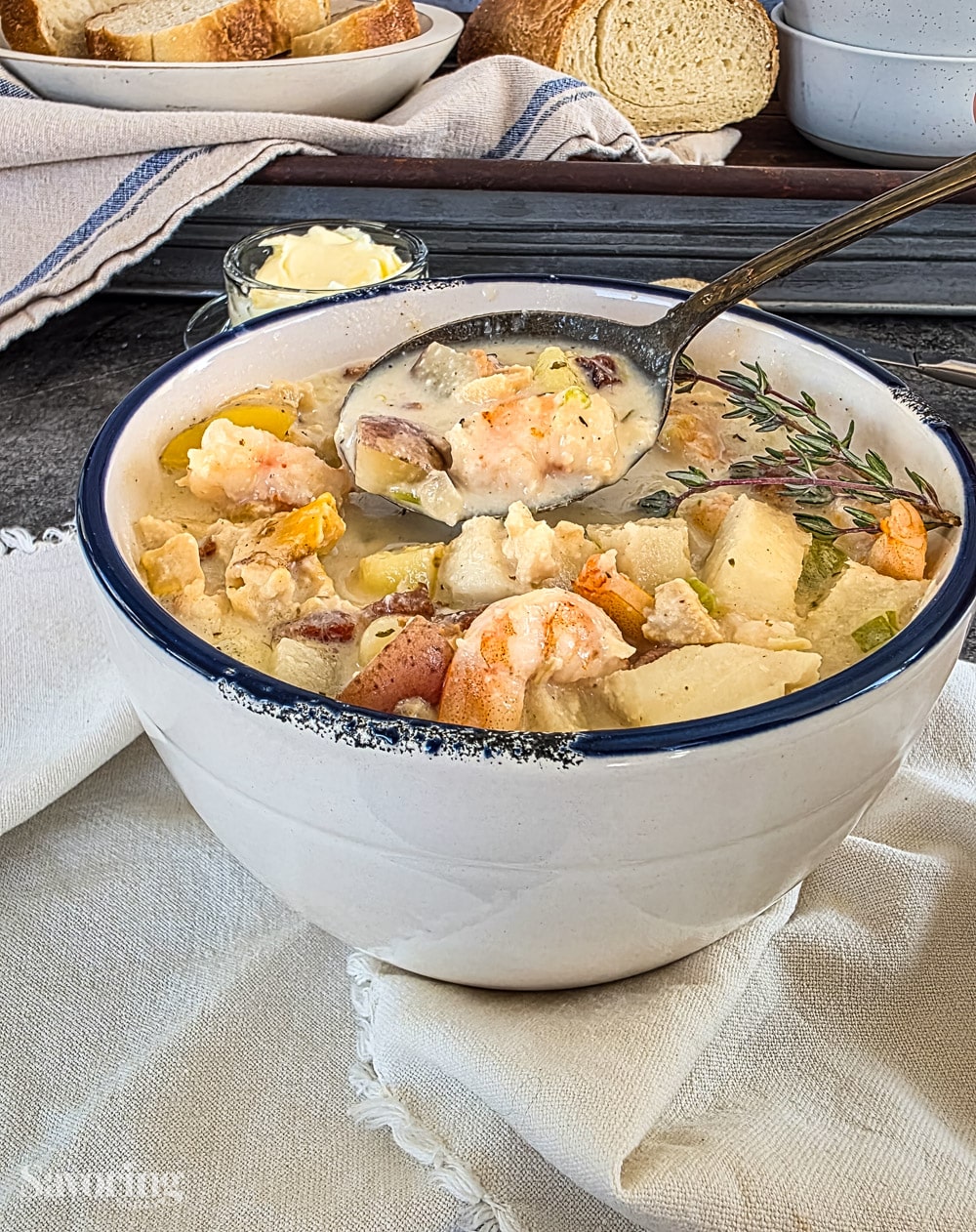 seafood chowder in a white bowl with a navy blue rim on a linen napkin