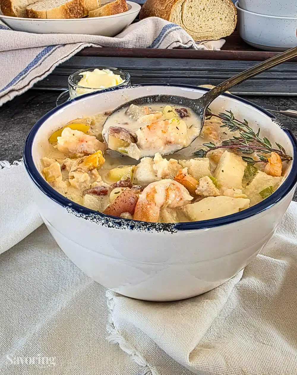 seafood chowder in a white bowl with a navy blue rim on a linen napkin