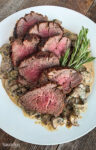 Grilled tenderloin on a bed of mushroom blue cheese sauce on a white plate