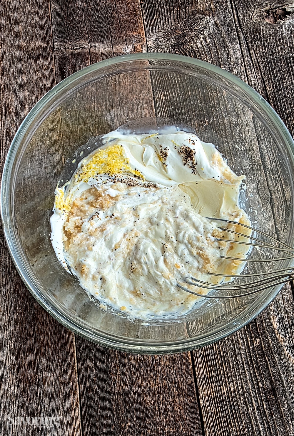 stirring horseradish yogurt sauce in a clear bowl with a whisk